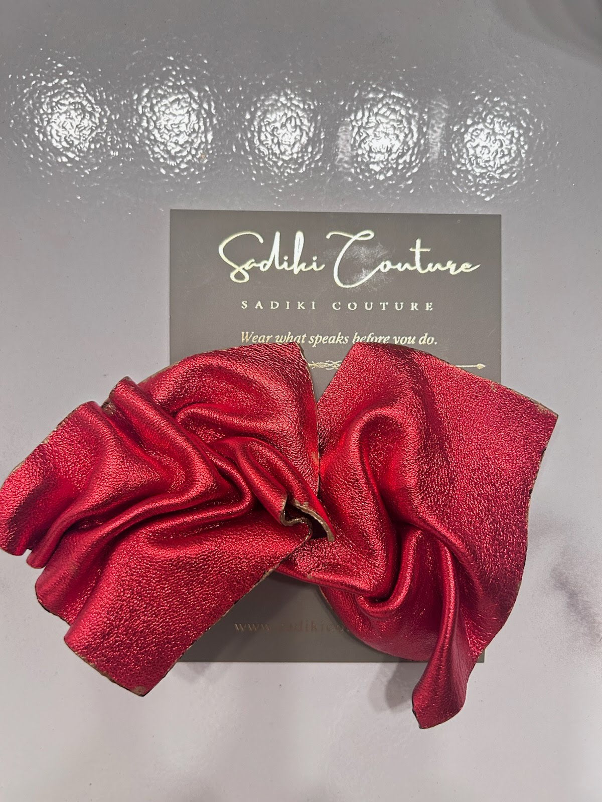 Red earrings with sculpted petal-like folds on a Sadiki Couture display card